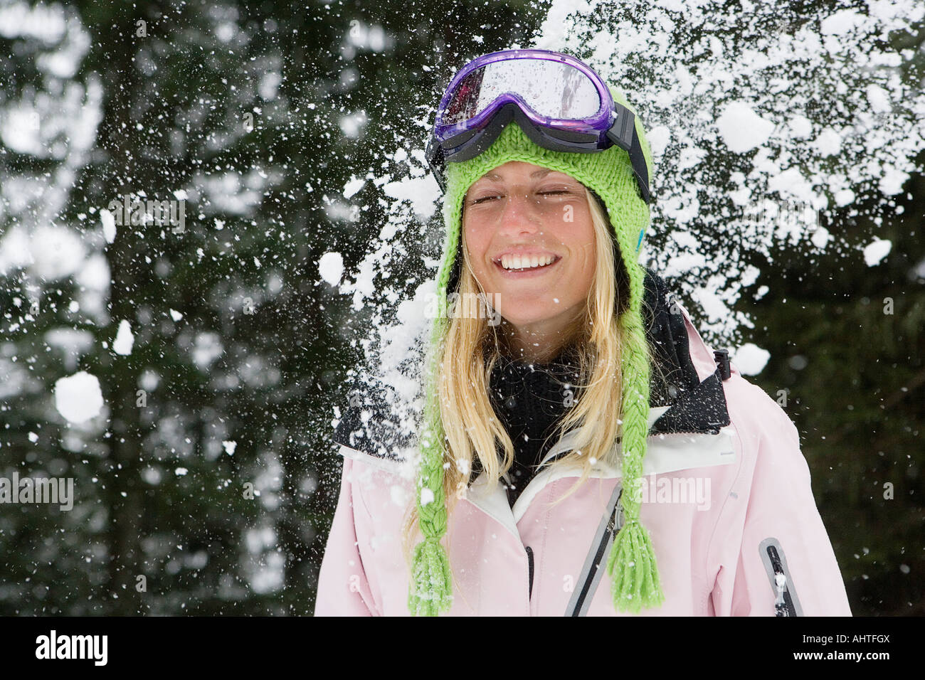 Snowball exploding on young blonde woman wearing ski-wear in forest Stock Photo