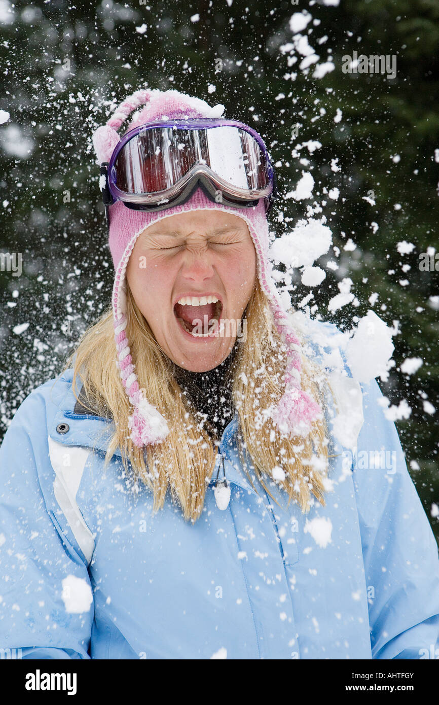 Snowball exploding on young blonde woman wearing ski-wear in forest Stock Photo