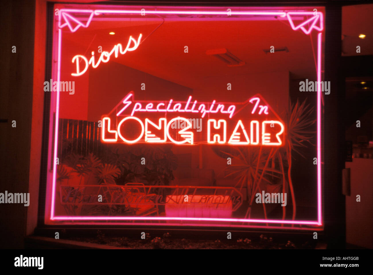 A neon sign that reads Dions specializing in long hair Stock Photo