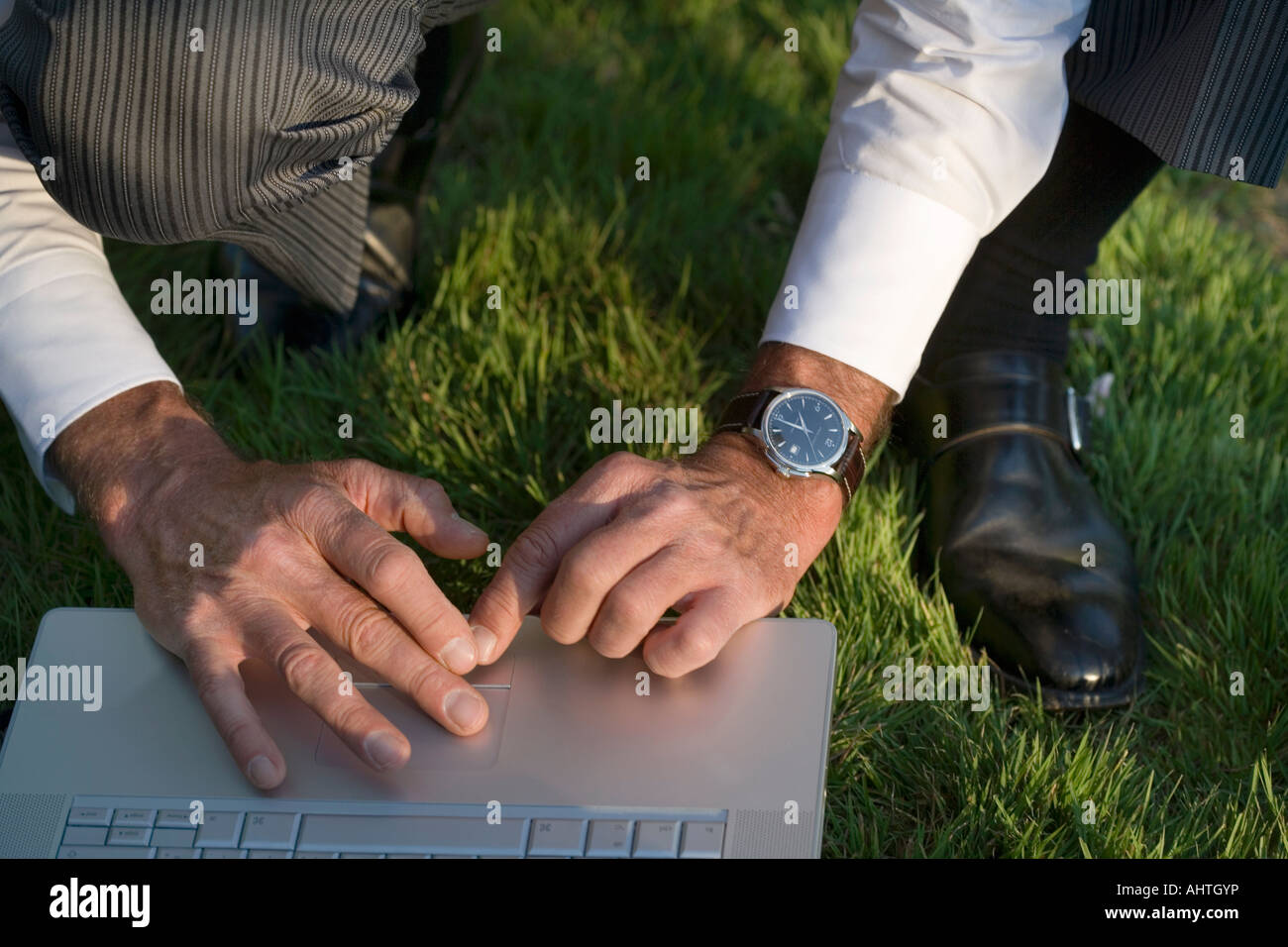 Man crouching on grass using laptop, close-up Stock Photo