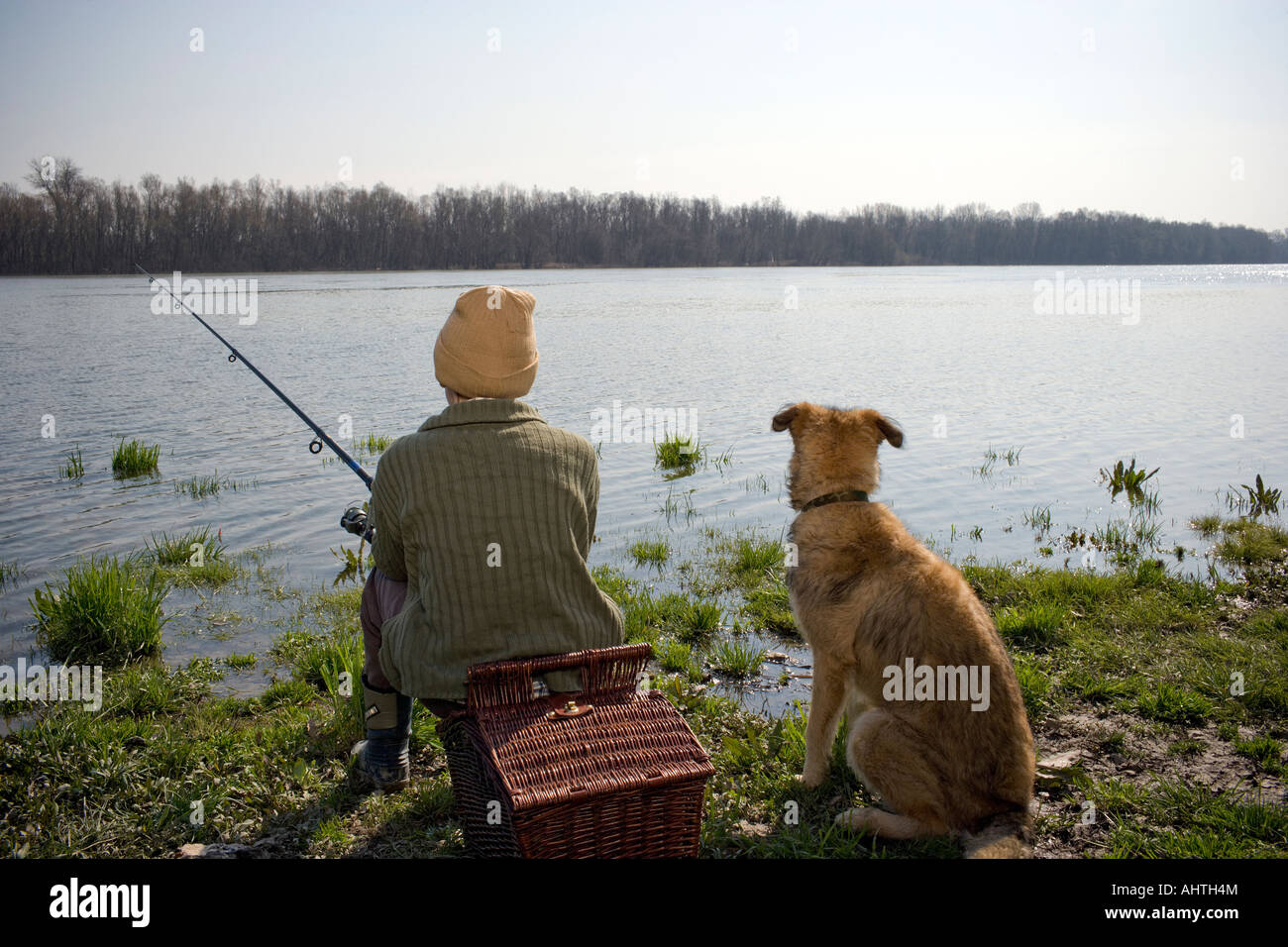 Boy (12-14) fishing by river with pet dog, rear view Stock Photo
