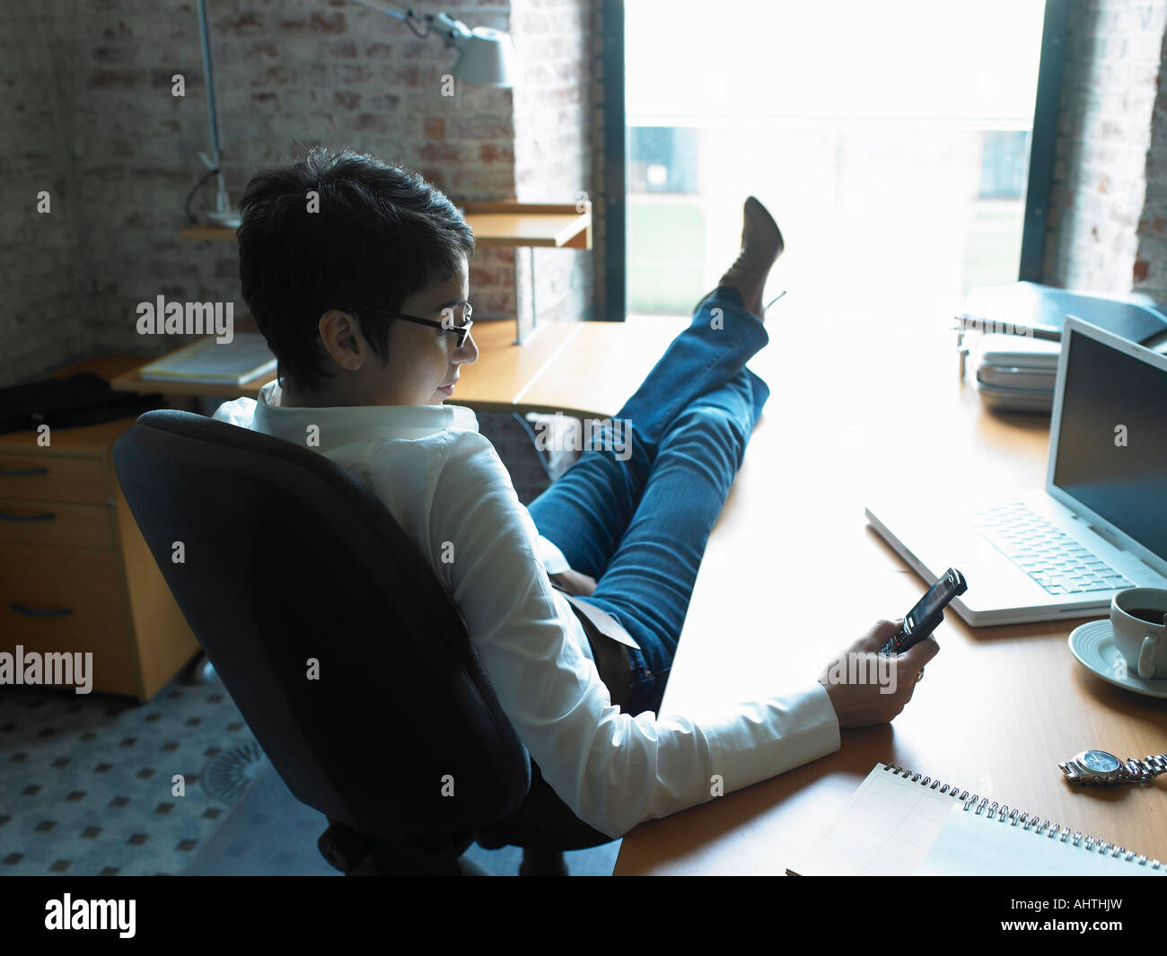 Rear view of businesswoman reading messages on phone with feet up on