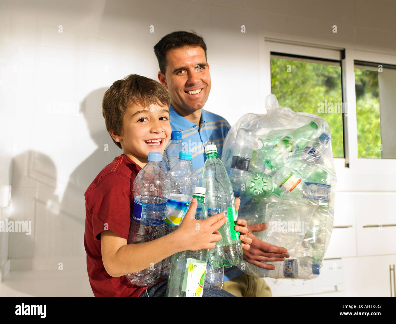 Father and son (6-8) recycling plastic bottles, smiling Stock
