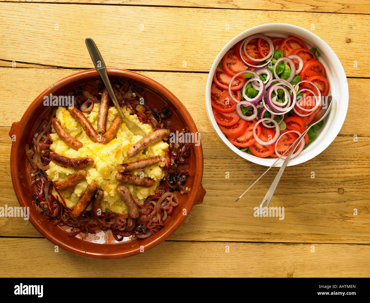 Sausage and mash with caramelized onions and tomato salad on wooden