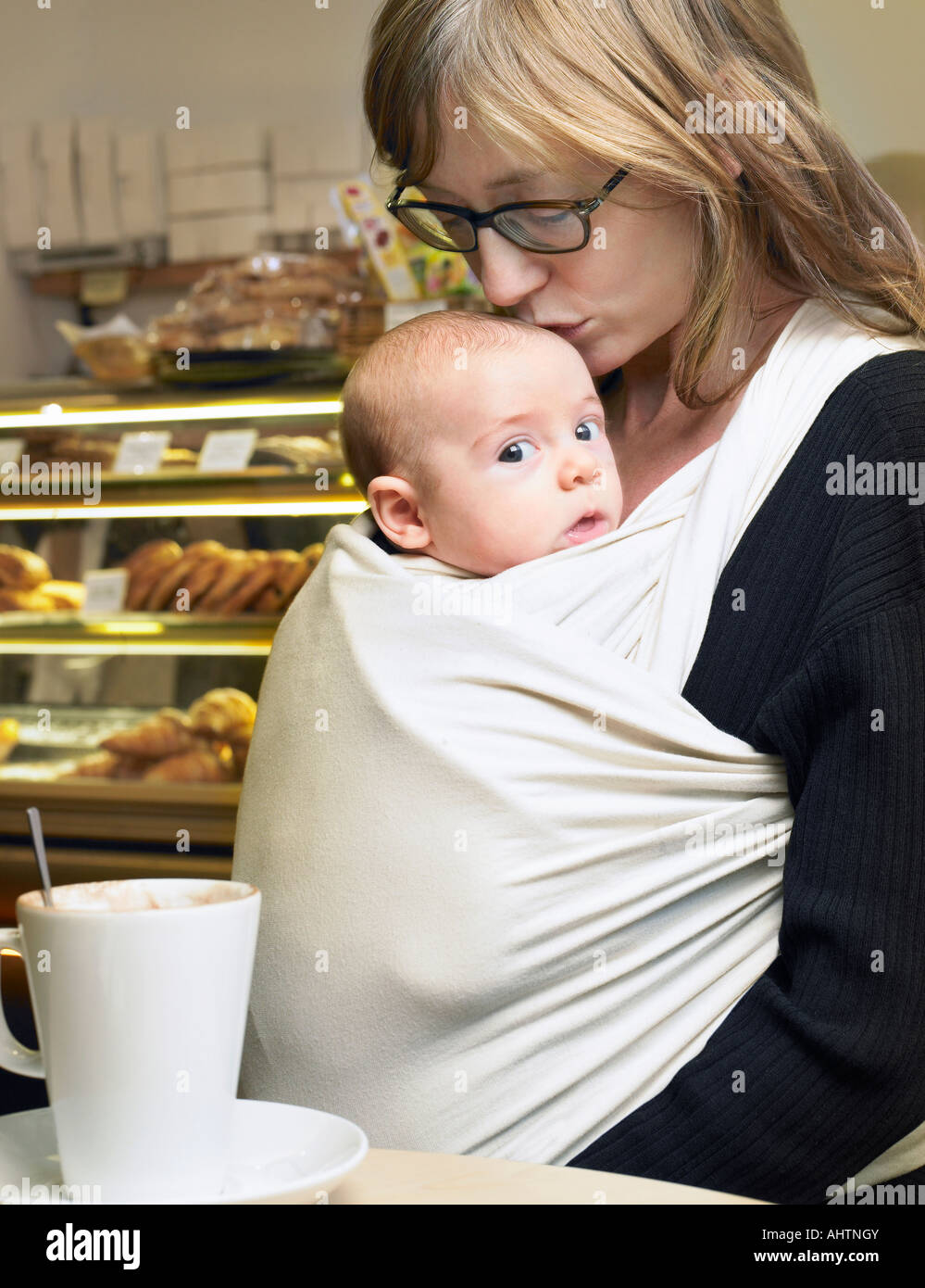 Mother kissing baby son (1-3 months) on head in cafe Stock Photo