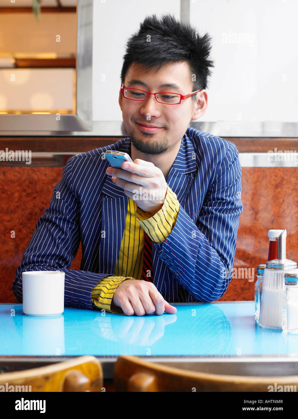 Young man sitting in cafe using mobile phone, smiling Stock Photo