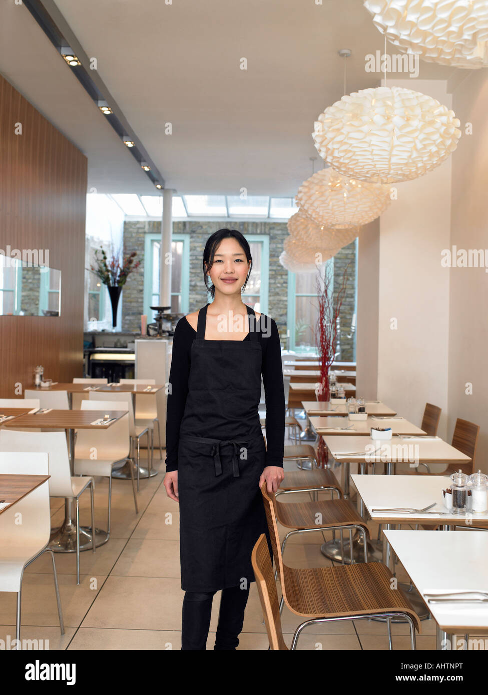Young waitress standing in empty restaurant, smiling, portrait Stock Photo