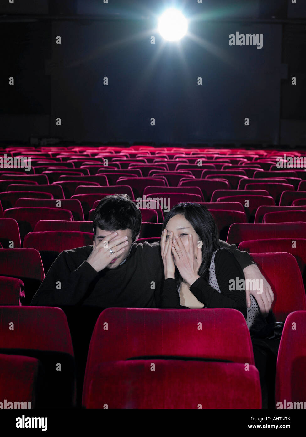 Young couple sitting in cinema holding hands over faces Stock Photo