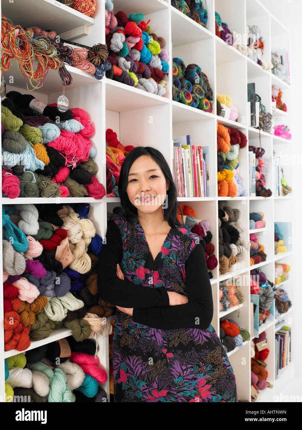 Young woman leaning on shelves of wool in craft shop, smiling Stock Photo