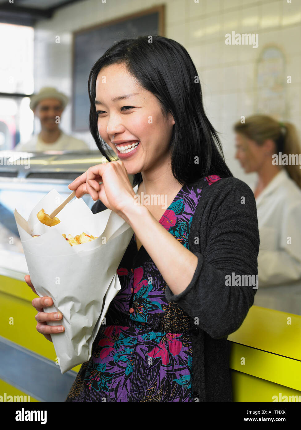 Young woman eating chips in fish and chip shop smiling Stock Photo