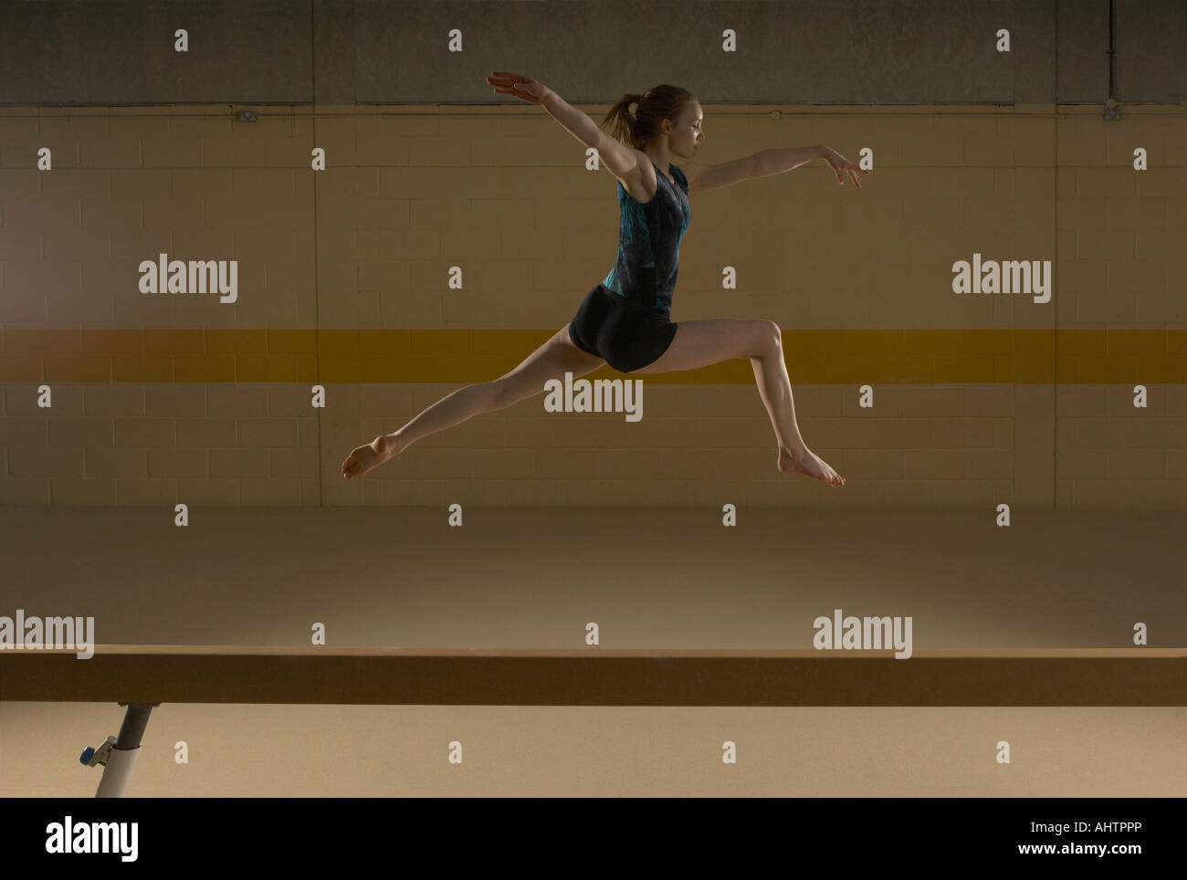 Teenage gymnast (16-18) leaping on balance beam Stock Photo