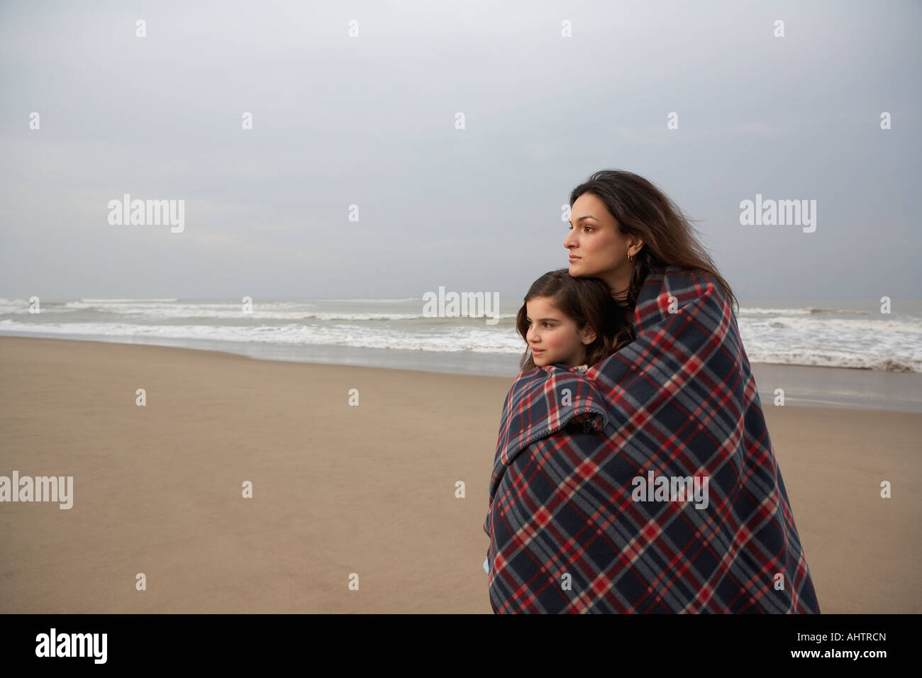 Mother and daughter (9-11) wrapped in blanket on beach Stock Photo