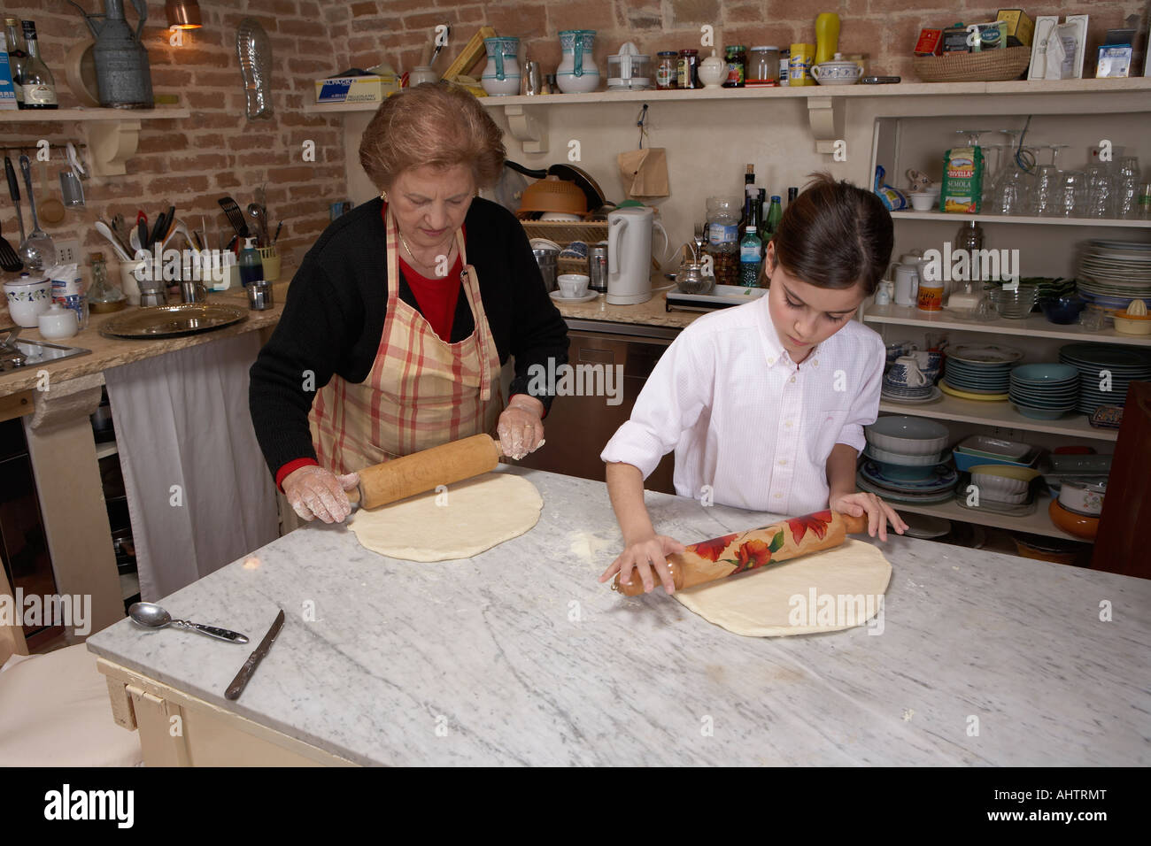 Senior woman and granddaughter (9-11) rolling pastry in kitchen Stock Photo