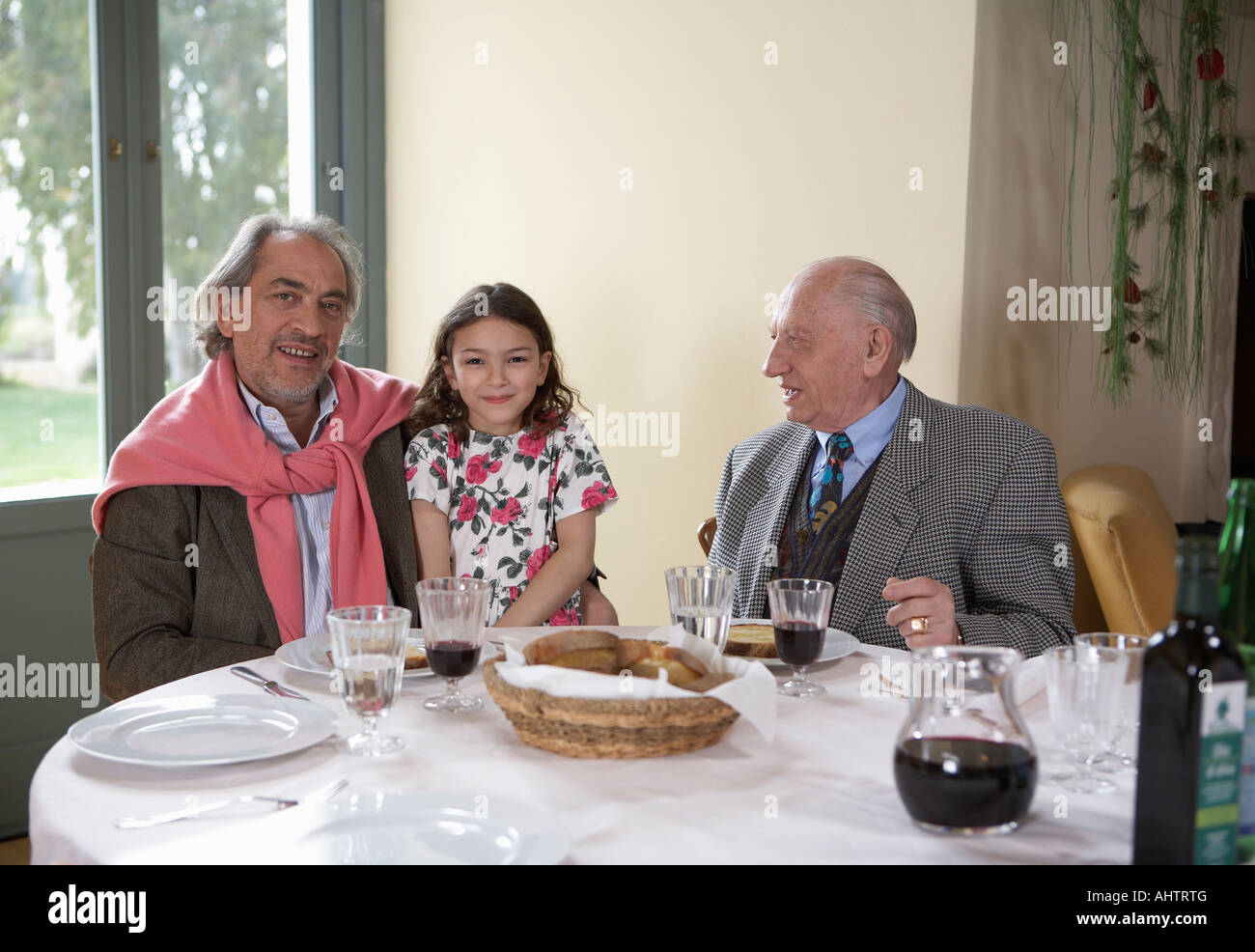 Girl (5-7) sitting with great-grandfather and grandfather at dinner table Stock Photo