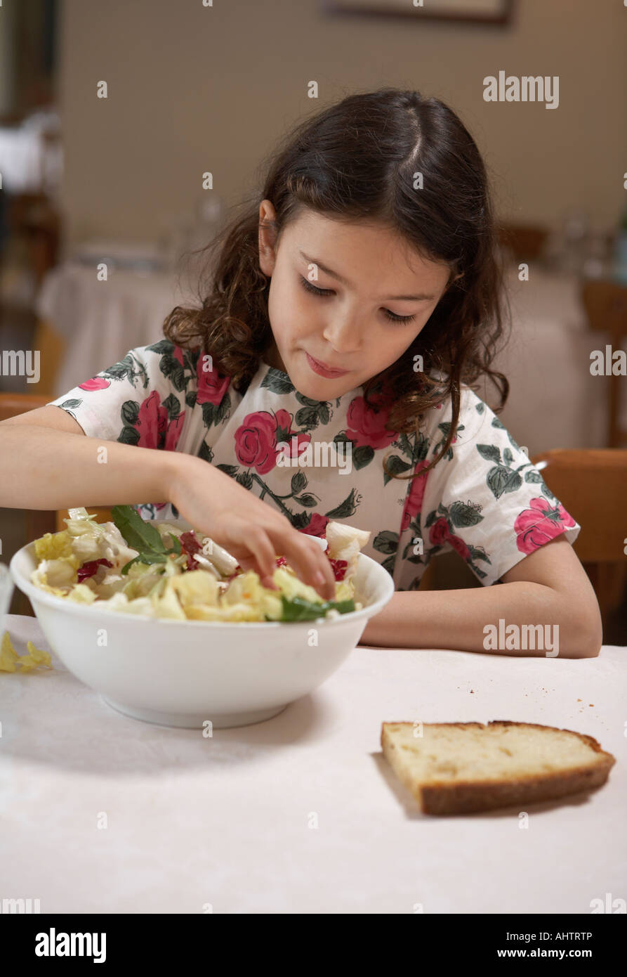 Girl (5-7) eating salad from bowl at a table Stock Photo
