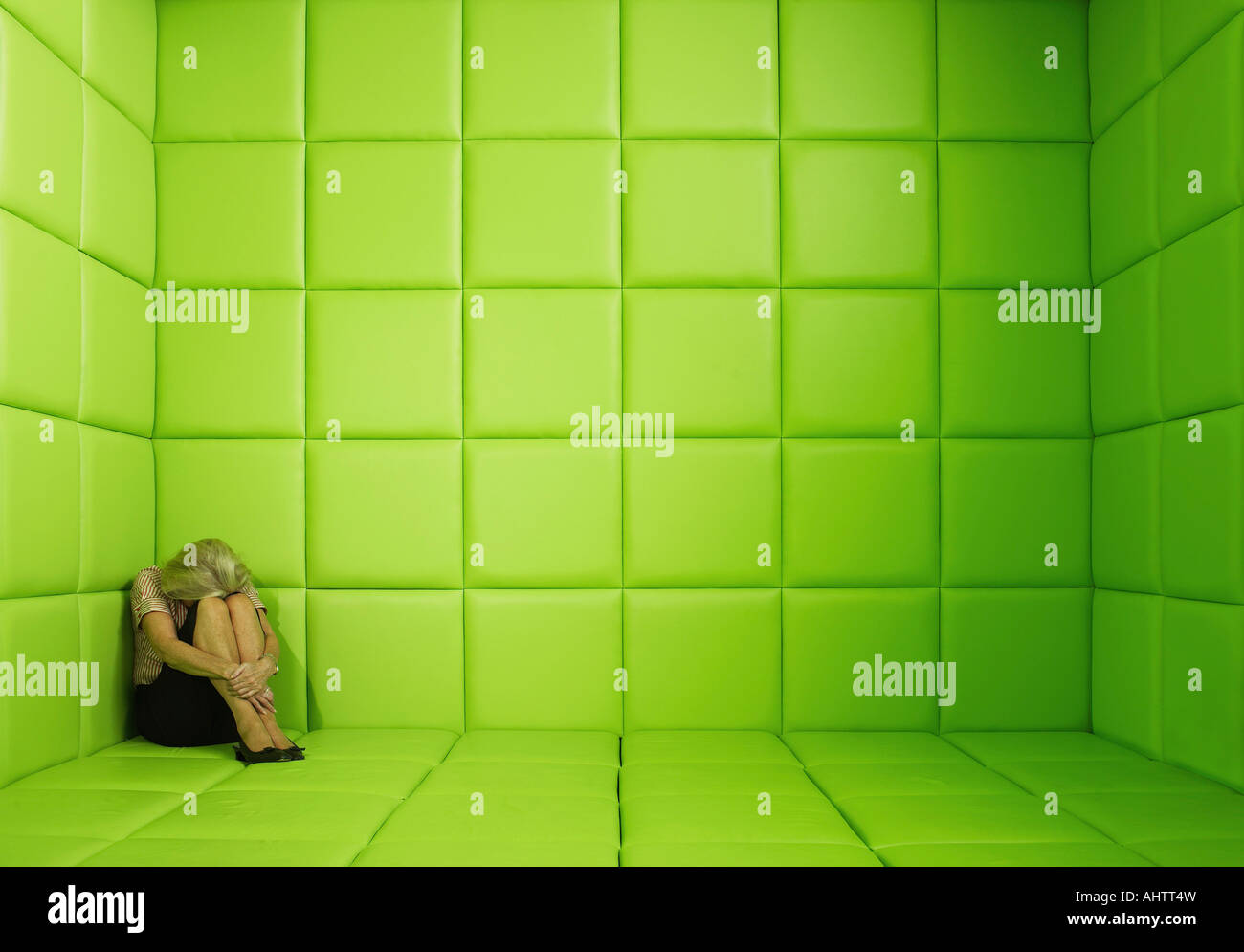Woman crouching in corner of green padded cell Stock Photo