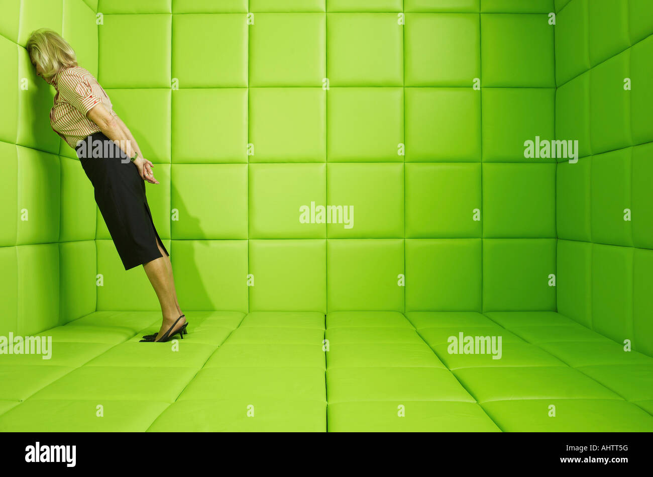 Woman leaning head against wall in a green padded cell Stock Photo