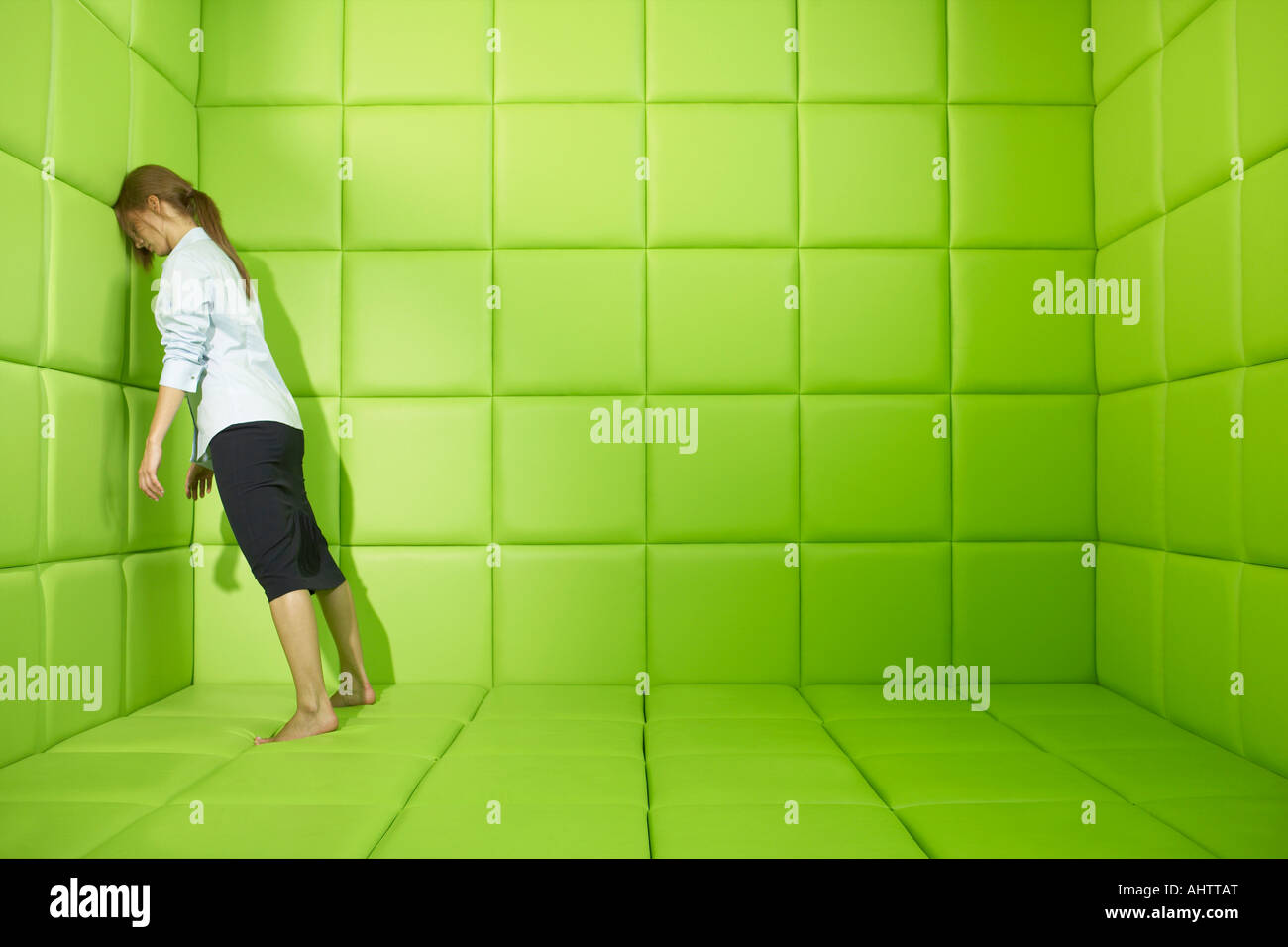 Woman pushing against walls of green padded cell Stock Photo