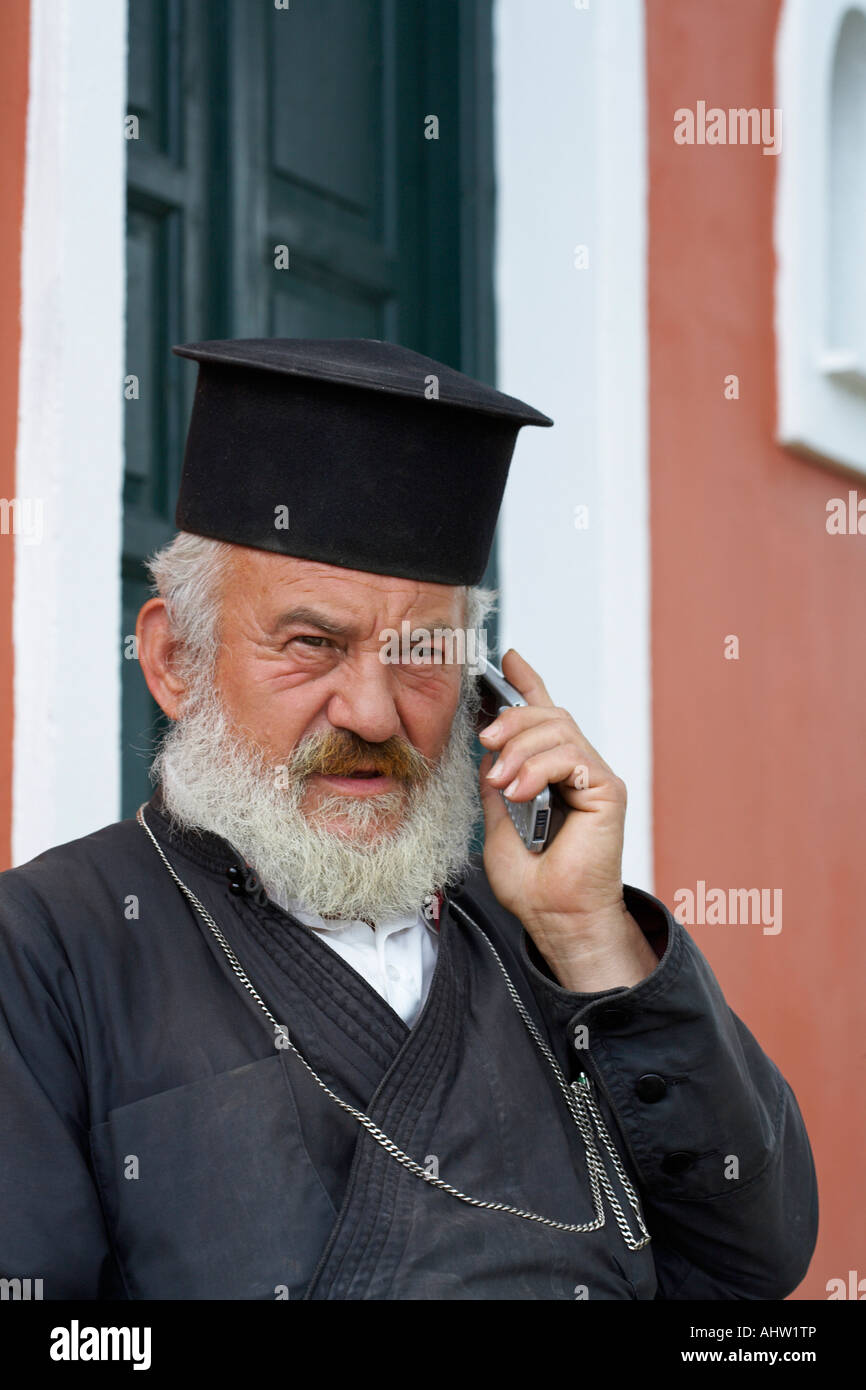 Old priest in front of church on the mobile. Stock Photo