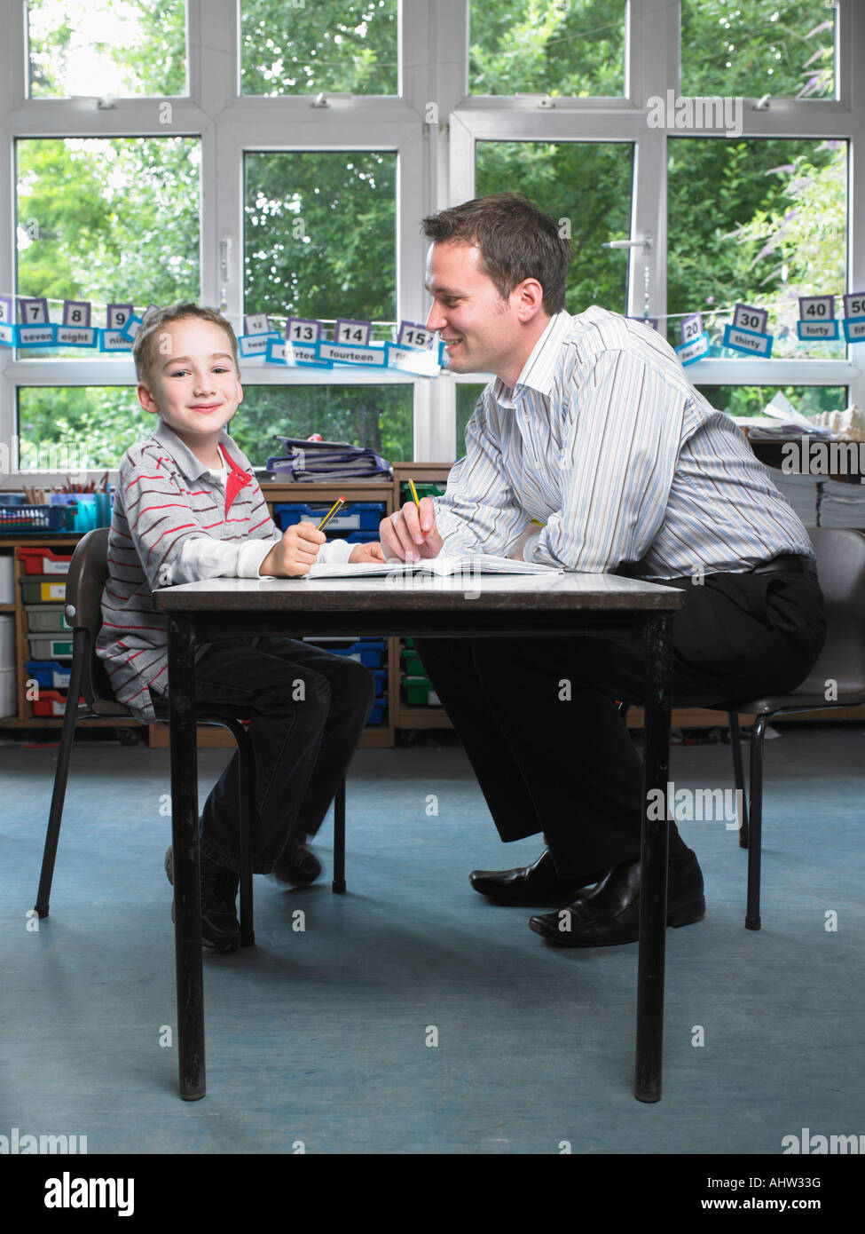 Male teacher helping young boy with work in classroom Stock Photo