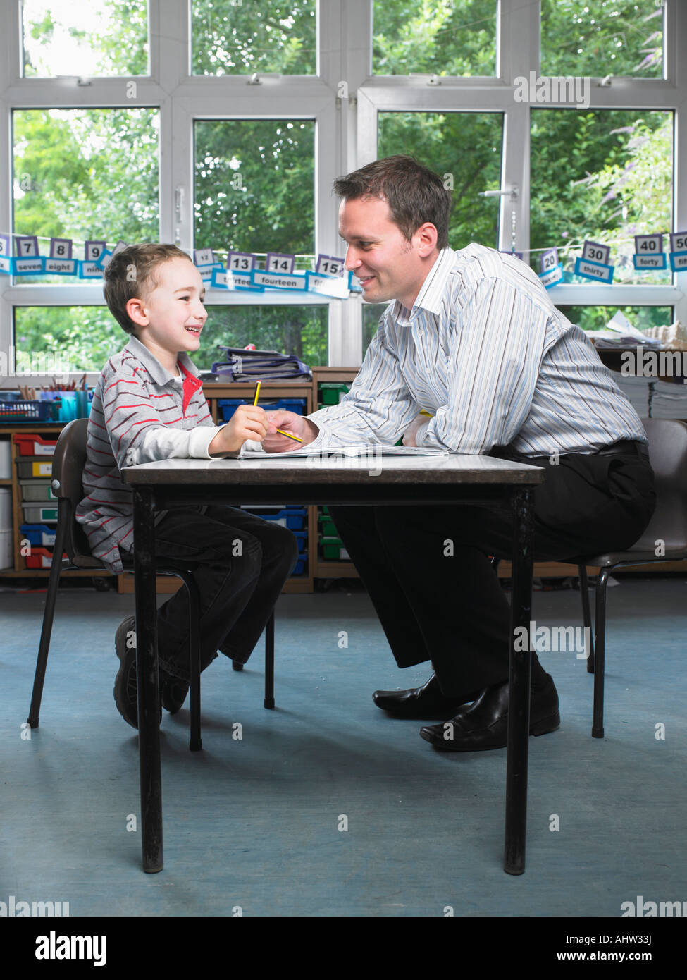 Male teacher helping young boy with work in classroom Stock Photo