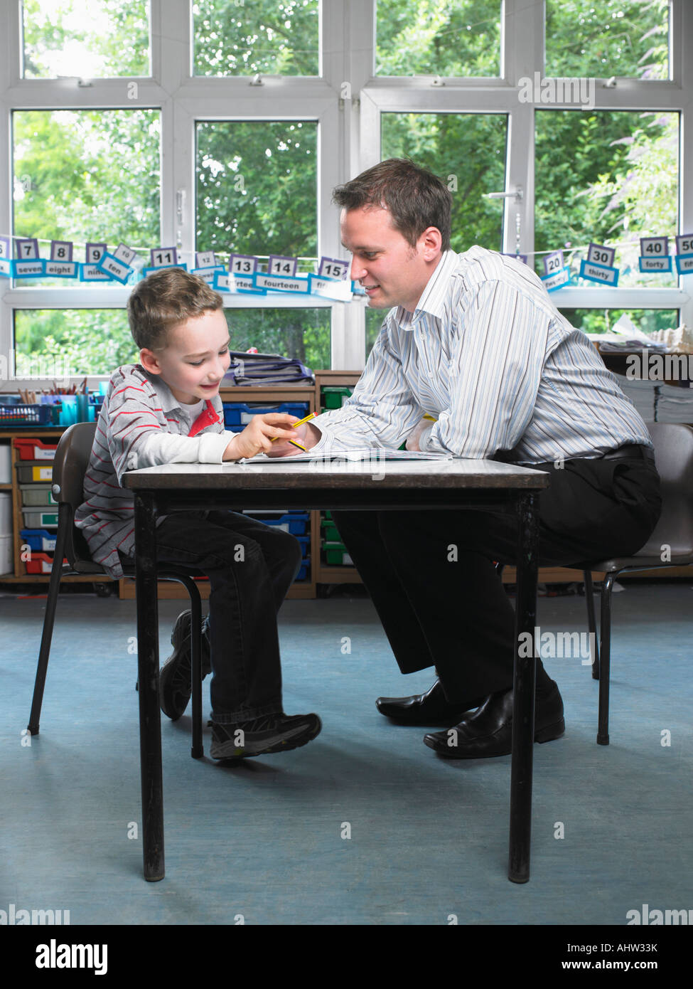 Male teacher helping young boy with work in classroom Stock Photo