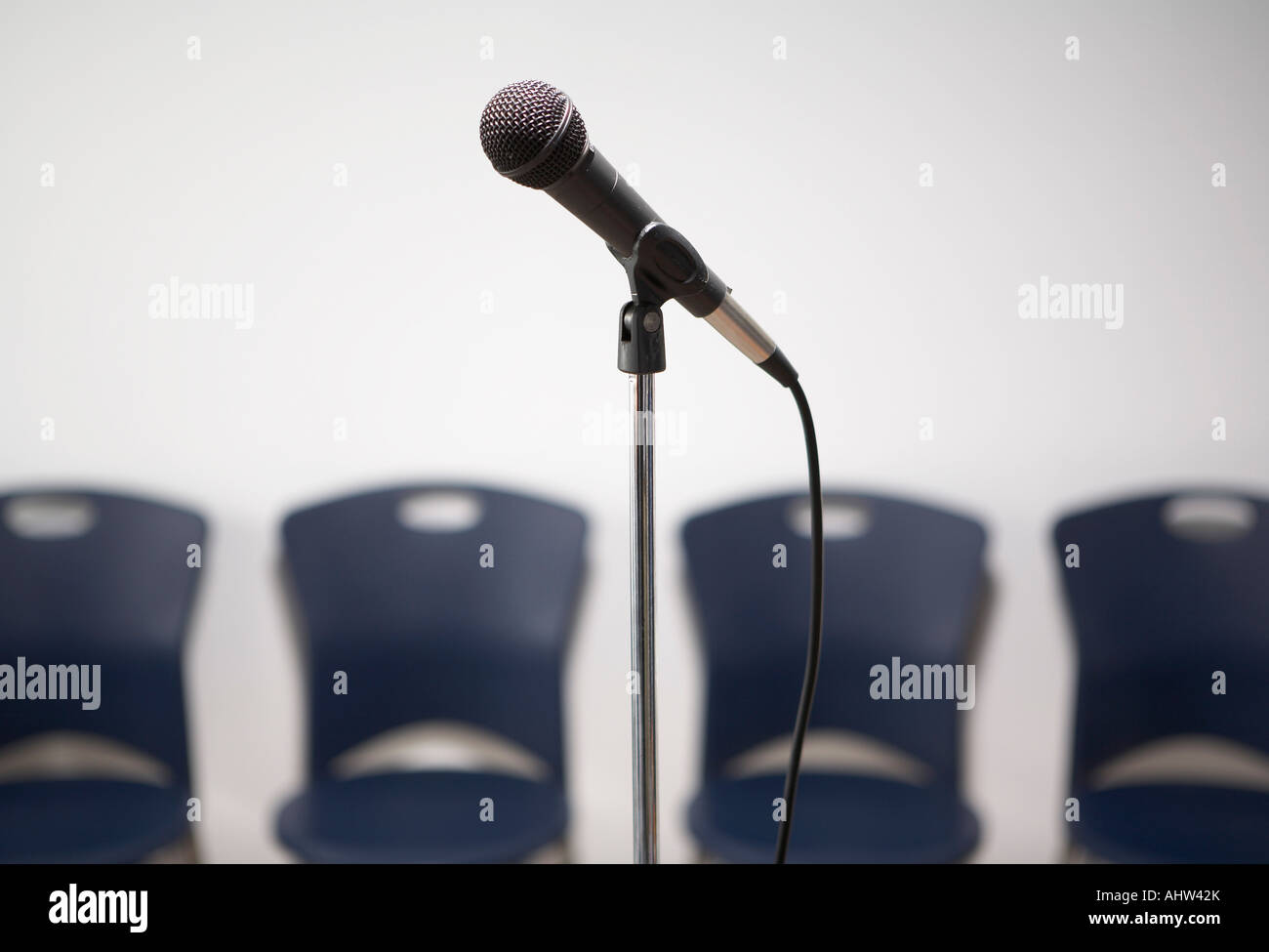 A microphone stand with chairs in the background. Stock Photo