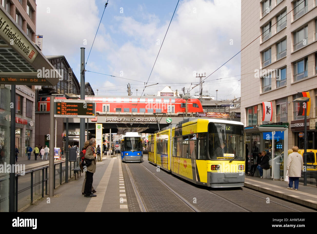 Horizontal wide angle cityscape of Friedrichstrasse with a train departing the station and two trams approaching their stops. Stock Photo