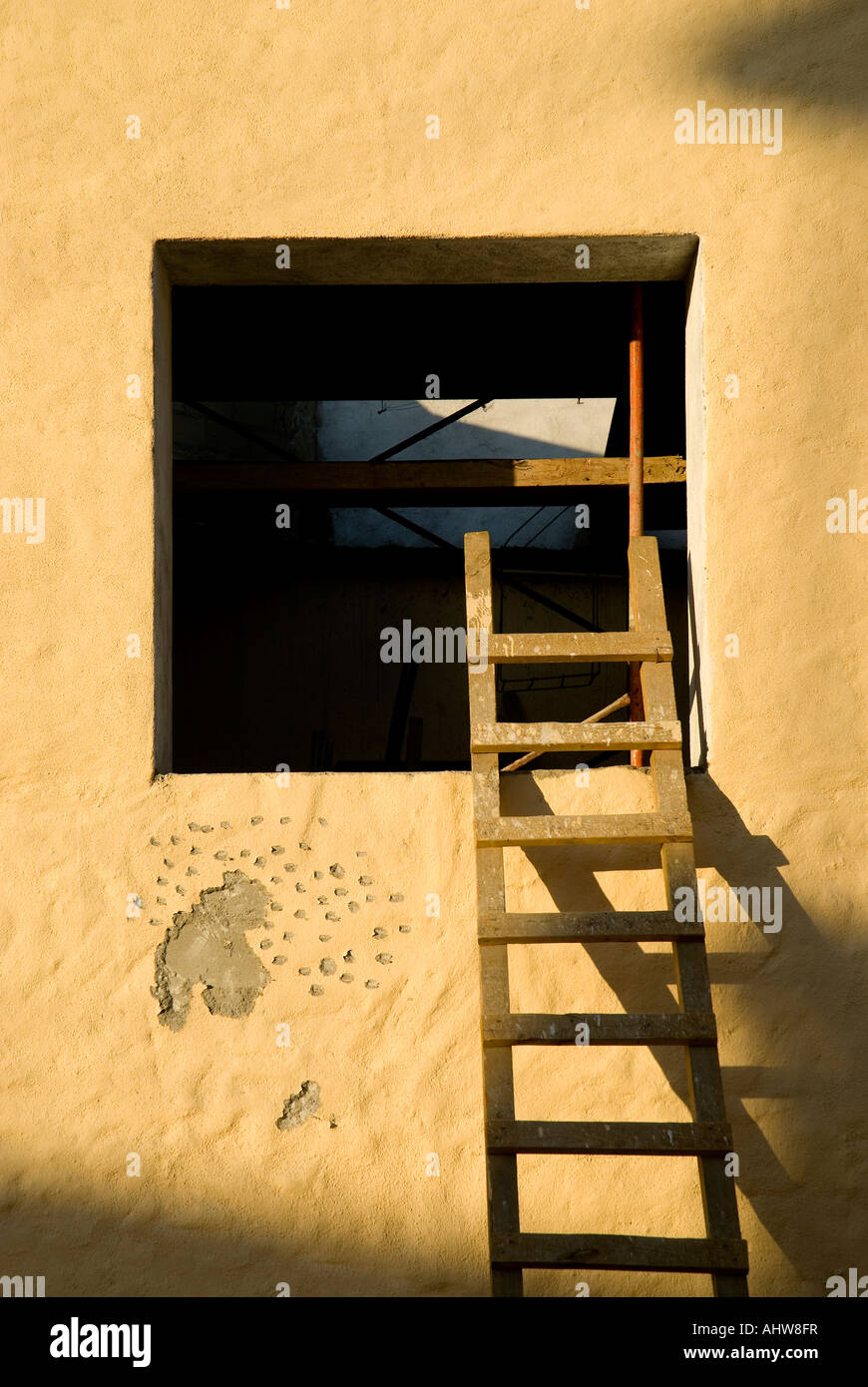 A colorful aged Mexican plaster window in twilight shadow with ladder ascending Stock Photo