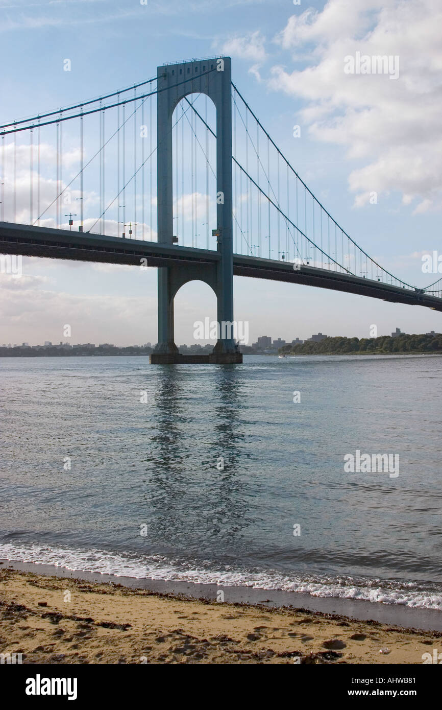 vertical shot of Whitestone Bridge in NYC showing bridge reflecting in the water taken from a beach with small waves lapping at Stock Photo