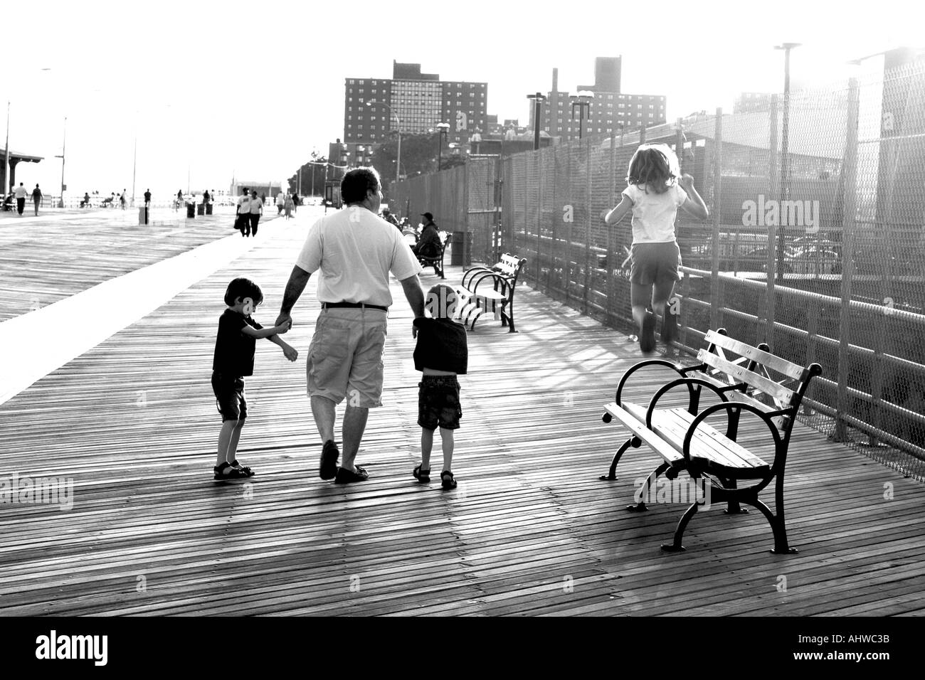 father and children strolling down the Coney Island boardwalk with the young girl daughter jumping off the benches as they walk Stock Photo