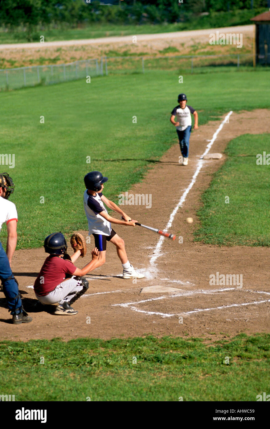 Little league action where the batter hits the ball and base runner is running Stock Photo