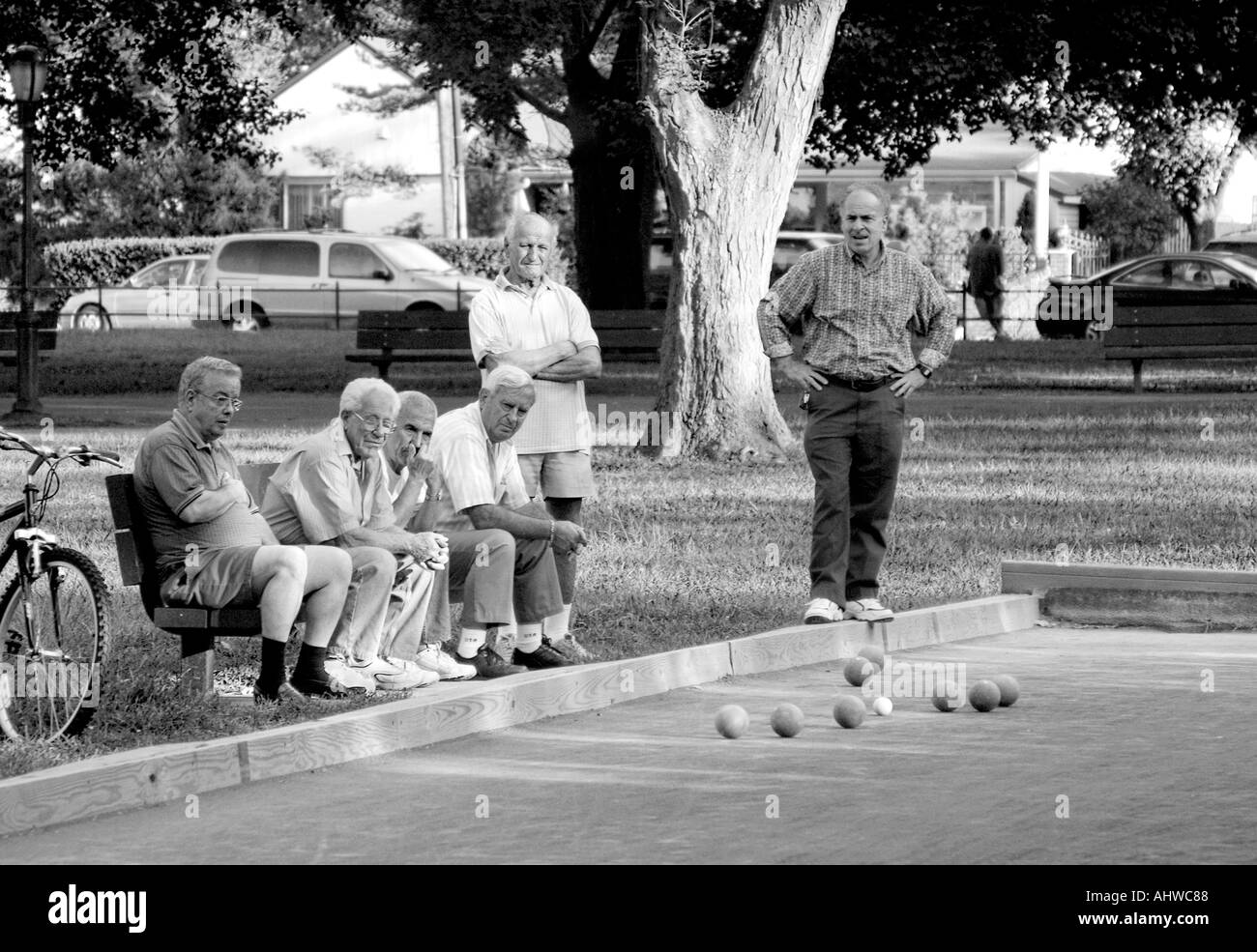 older senior men sitting on a park bench watching a bacci ball game in US Stock Photo