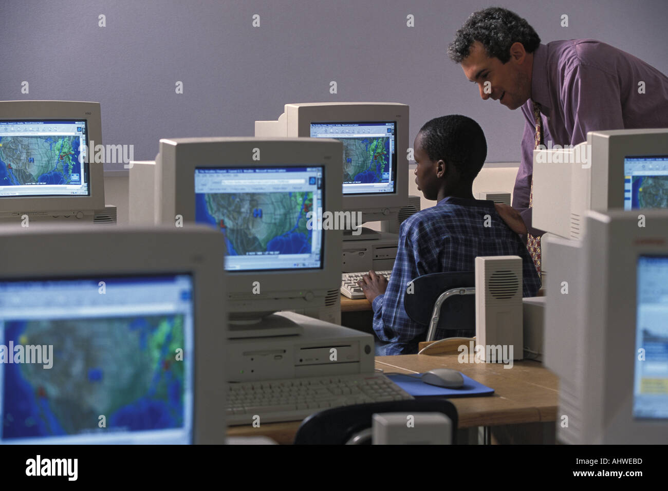 Caucasian male teacher helping African American student in middle school class Stock Photo