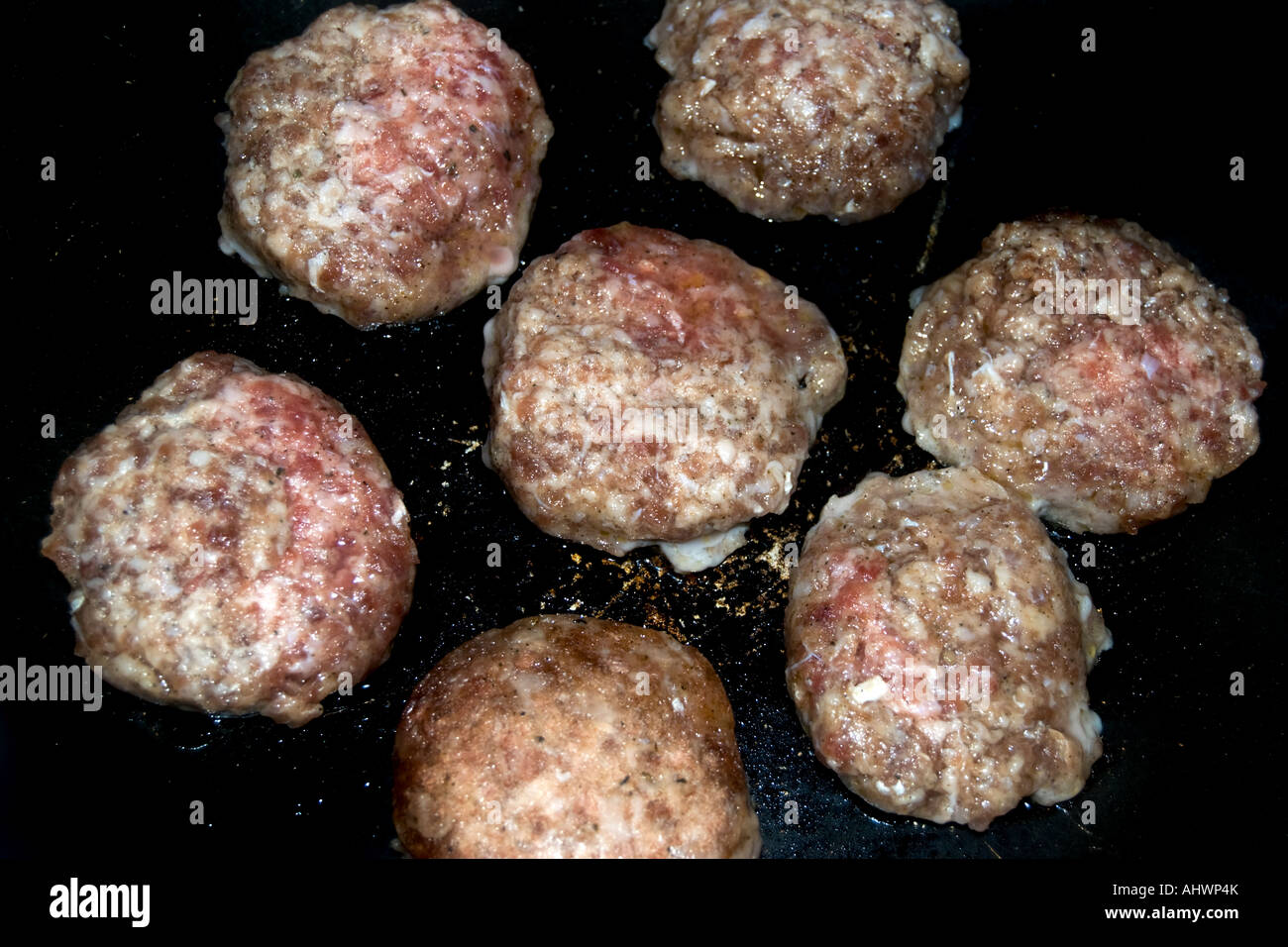 Seven patties of pork sausage cooking in a black frying pan Stock Photo