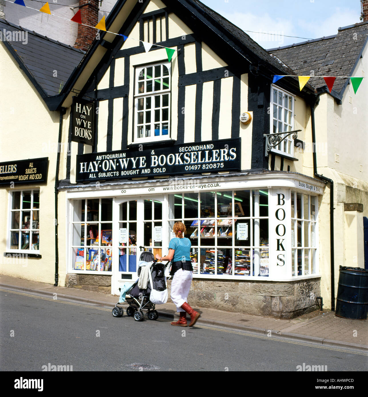 A woman with red boots and a pushchair buggy walking past Hay on Wye Booksellers shop selling books book town Wales UK Great Britain   KATHY DEWITT Stock Photo