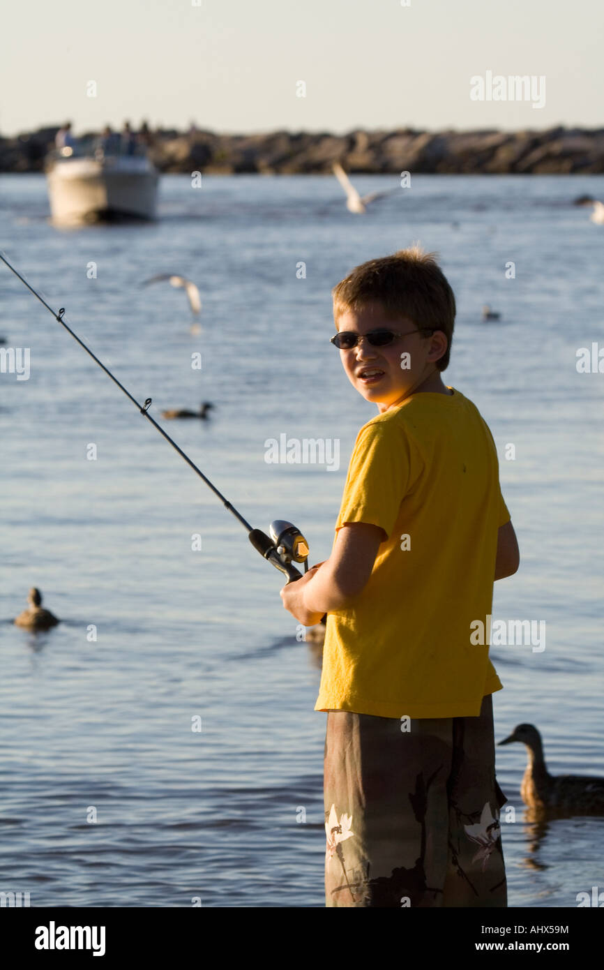 Young boy fishing alone by the water looking back over his shoulder Stock Photo