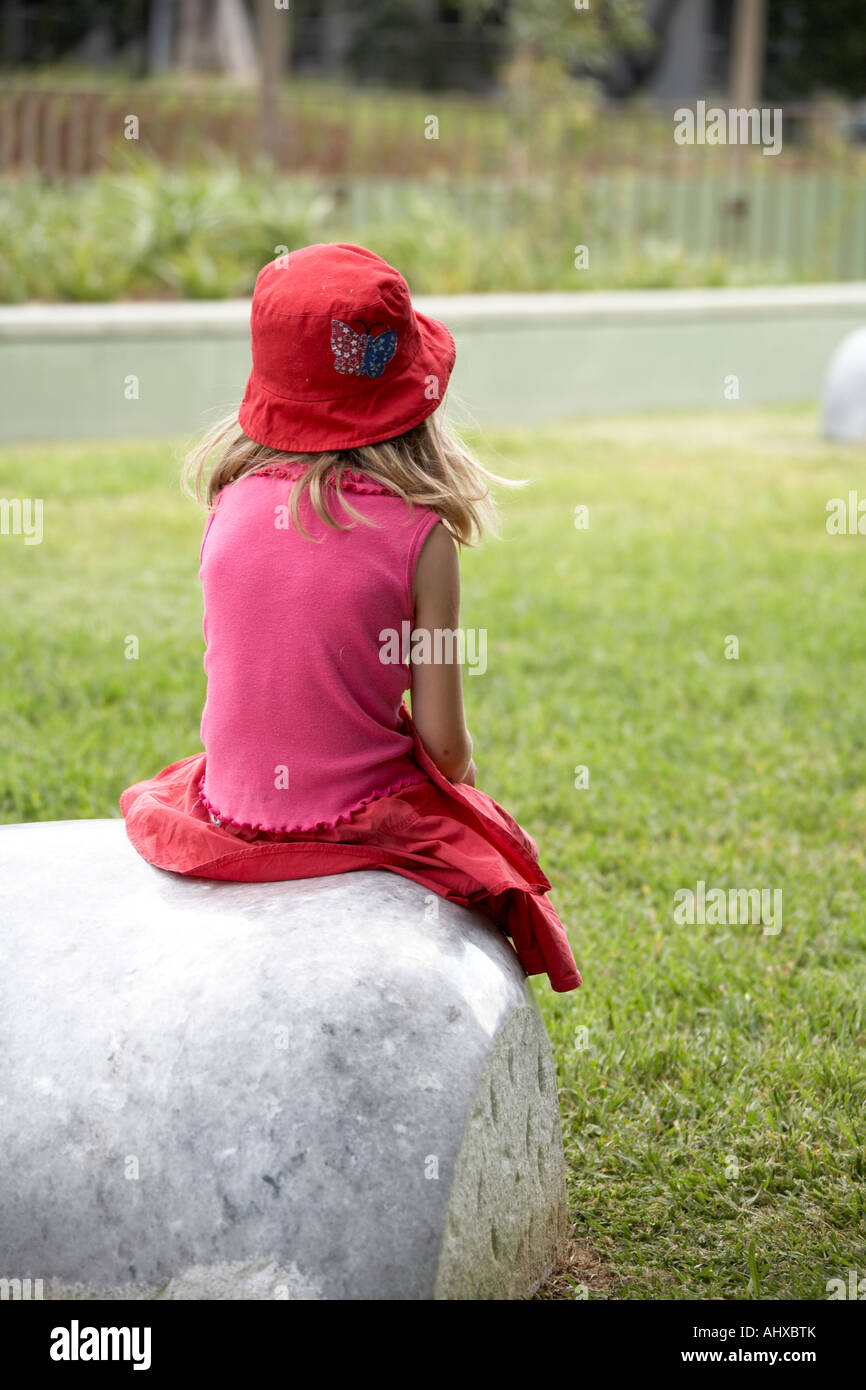 Young girl in red dress and hat sitting on a stone in Brisbane Queensland QLD Australia Stock Photo