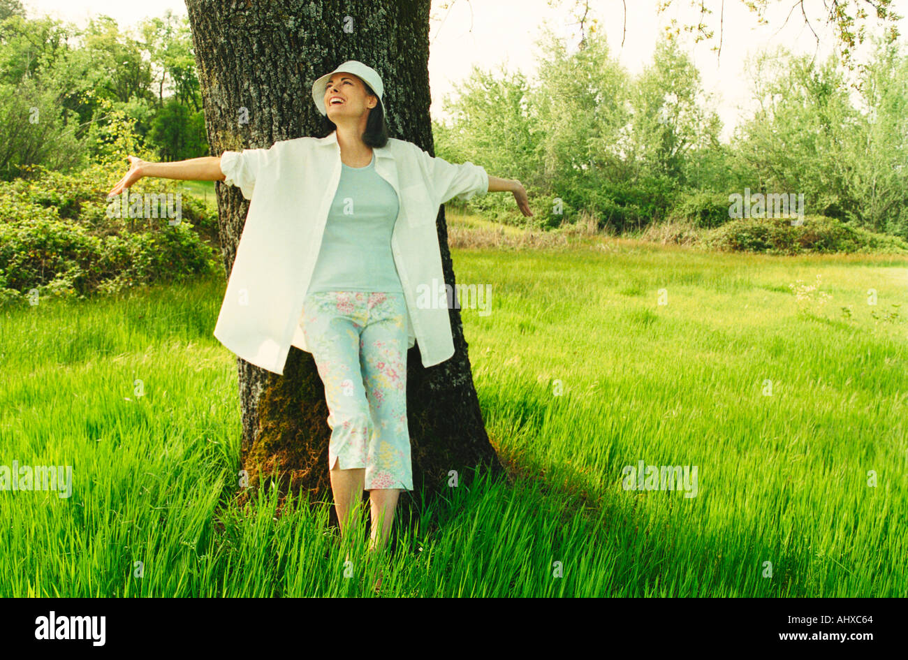 Expressive woman leaning against tree in field Stock Photo
