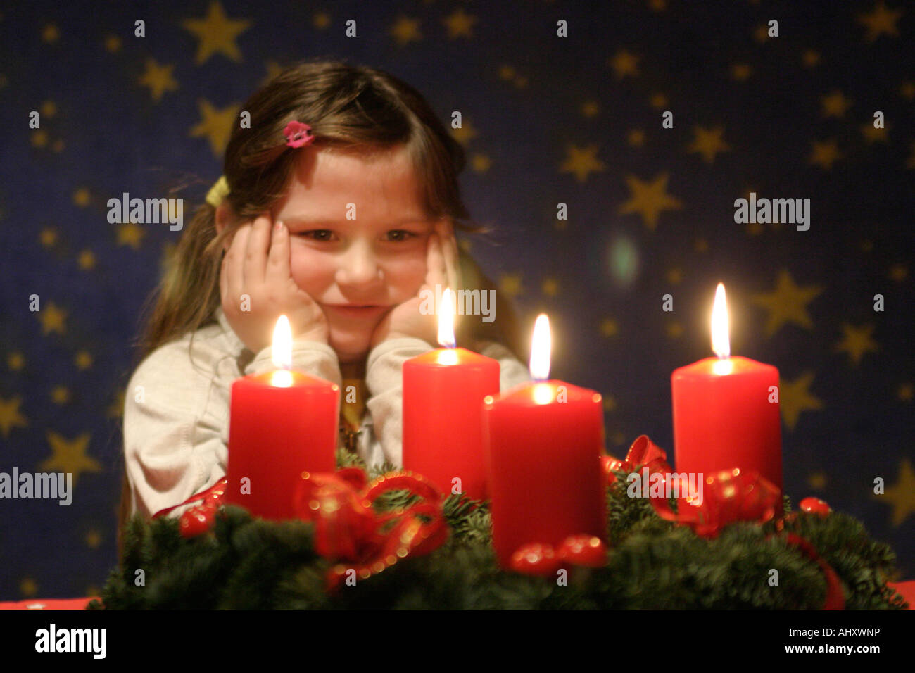 young girl looking at the candles of an Advent wreath happily Stock Photo