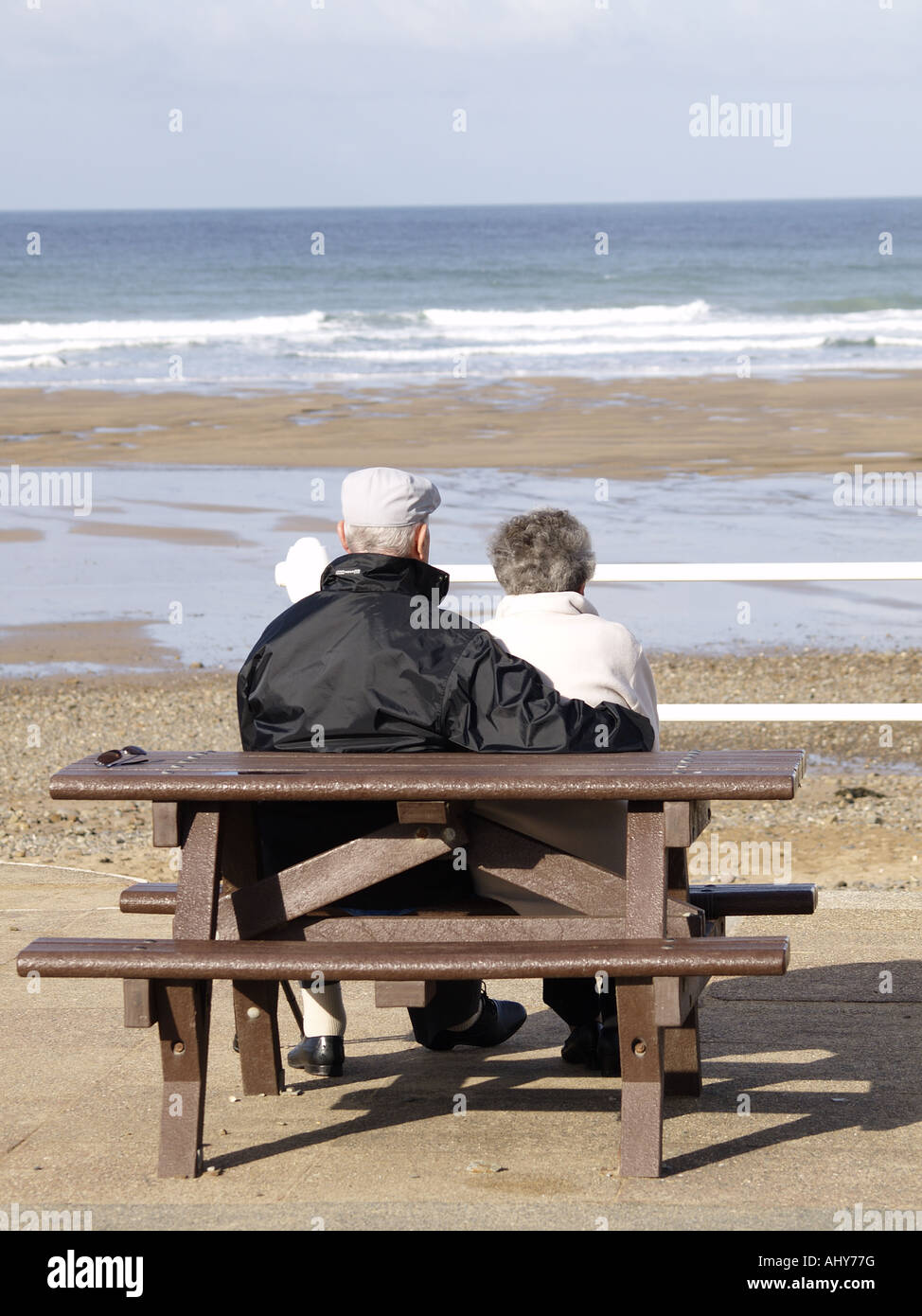 Old couple sitting on a wooden picnic bench at Crooklets beach, looking ...