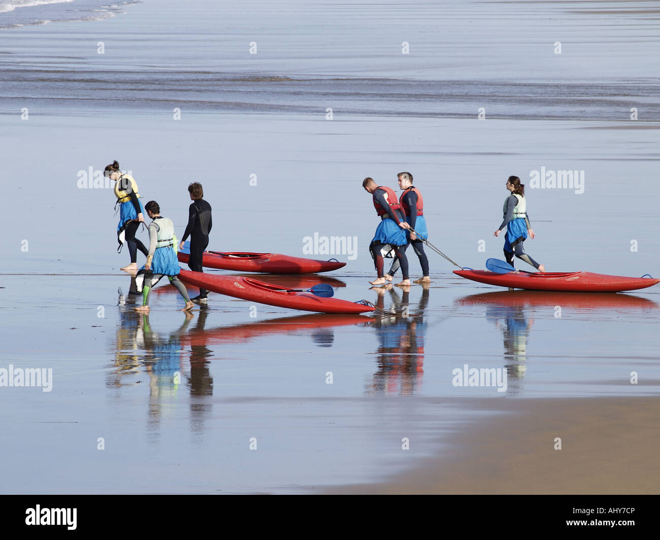 Group of 6 people pulling their kayaks along the beach towards the sea. Stock Photo