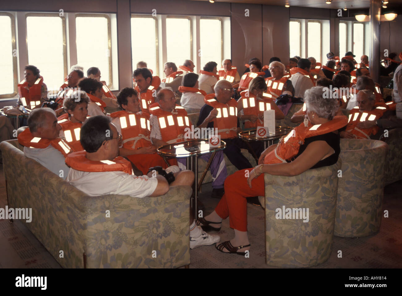 On board cruise ship liner crowd passengers wearing life jackets seated