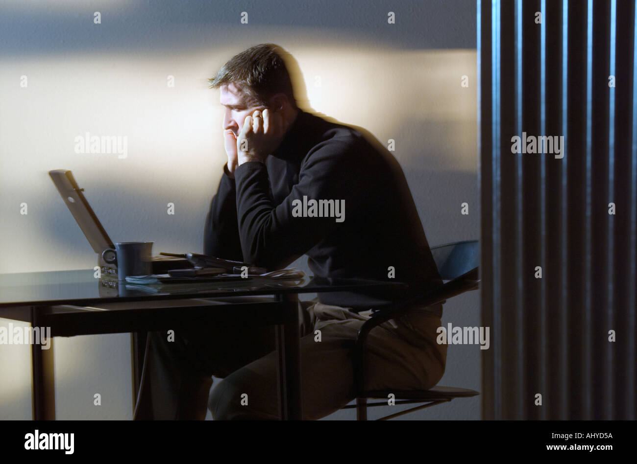 Perplexed man sitting at desk and using laptop computer Stock Photo