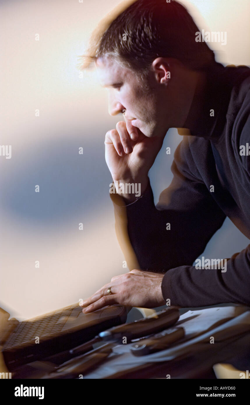 Thouhtful Caucasian man sitting at desk using laptop computer Stock Photo
