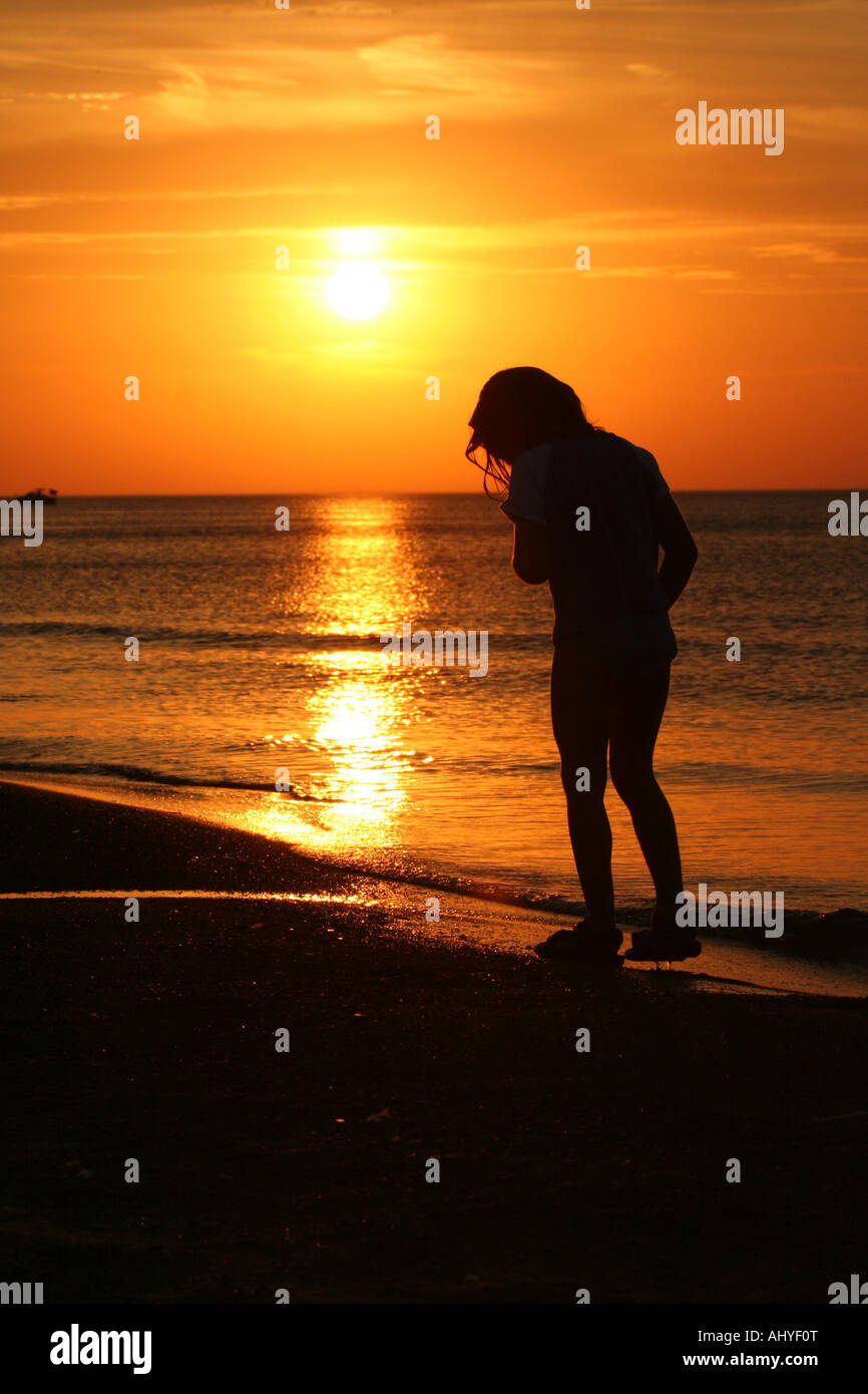 Silhouette of little girl walking on beach at sunset Stock Photo