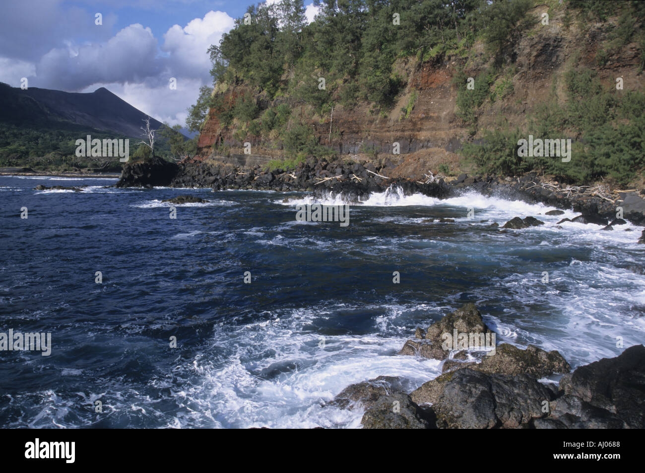 Rocky cliffs on the shore with Yasur Volcano visible in the background, Tanna Island, Vanuatu. Stock Photo