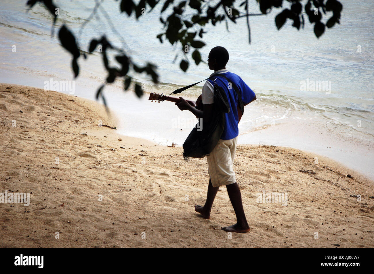 Mauritian man strolling along beach playing guitar. Pereybere, Mauritius. Stock Photo