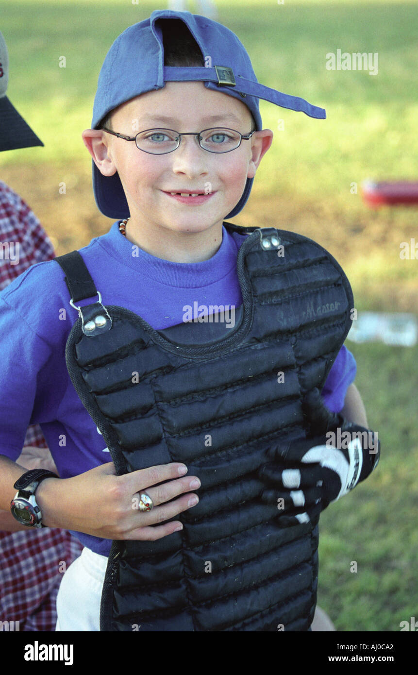Portrait of a smiling boy in a Little League baseball catcher uniform standing off field between innings Stock Photo