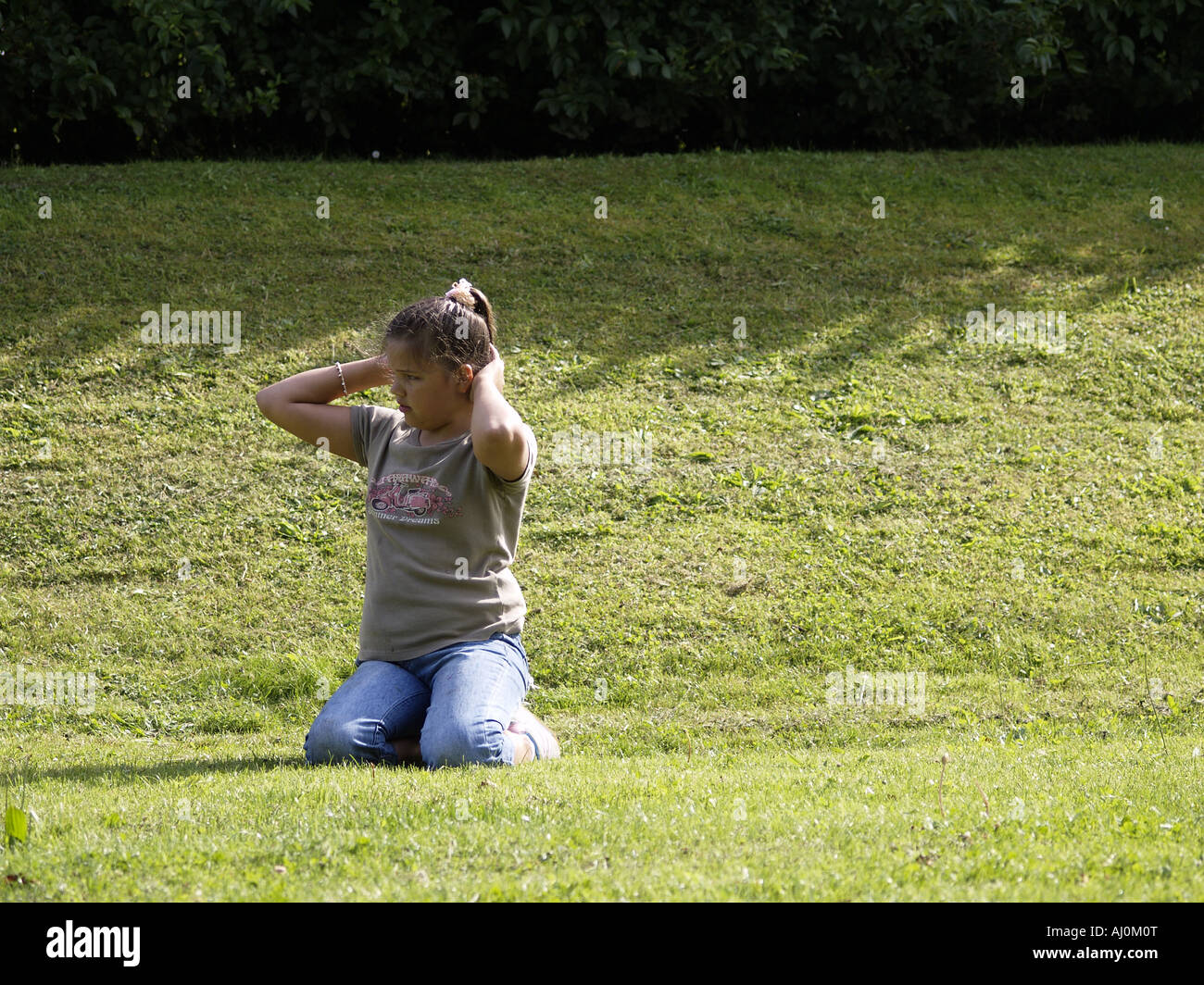 Teenage girl sitting on grass, fussing with her hair Stock Photo